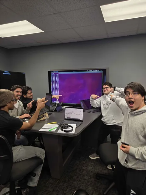 Members around a conference table pointing at a screen full of hello world output